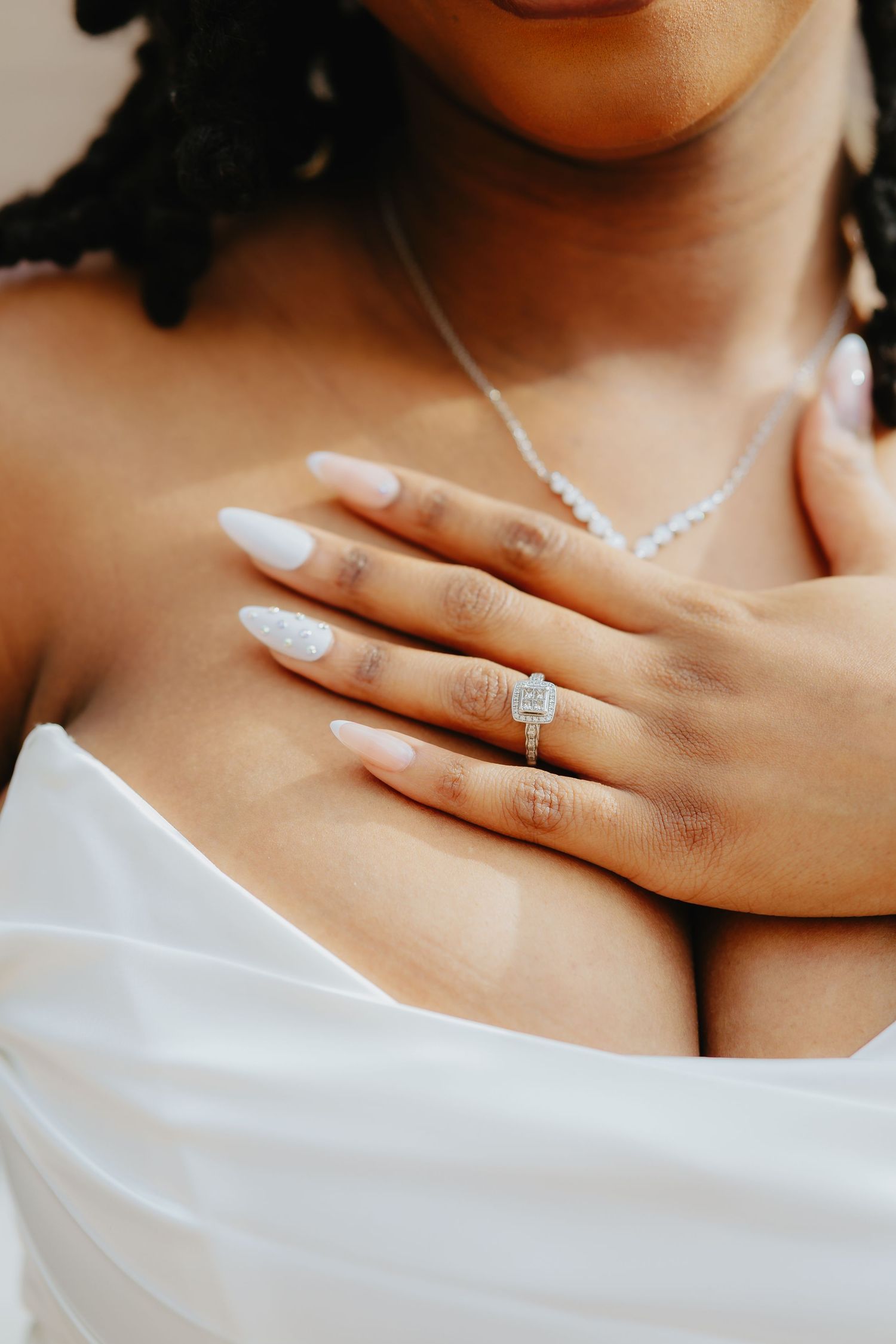 Close-up of elegant bridal jewelry featuring a delicate necklace and statement diamond ring with white manicured nails.