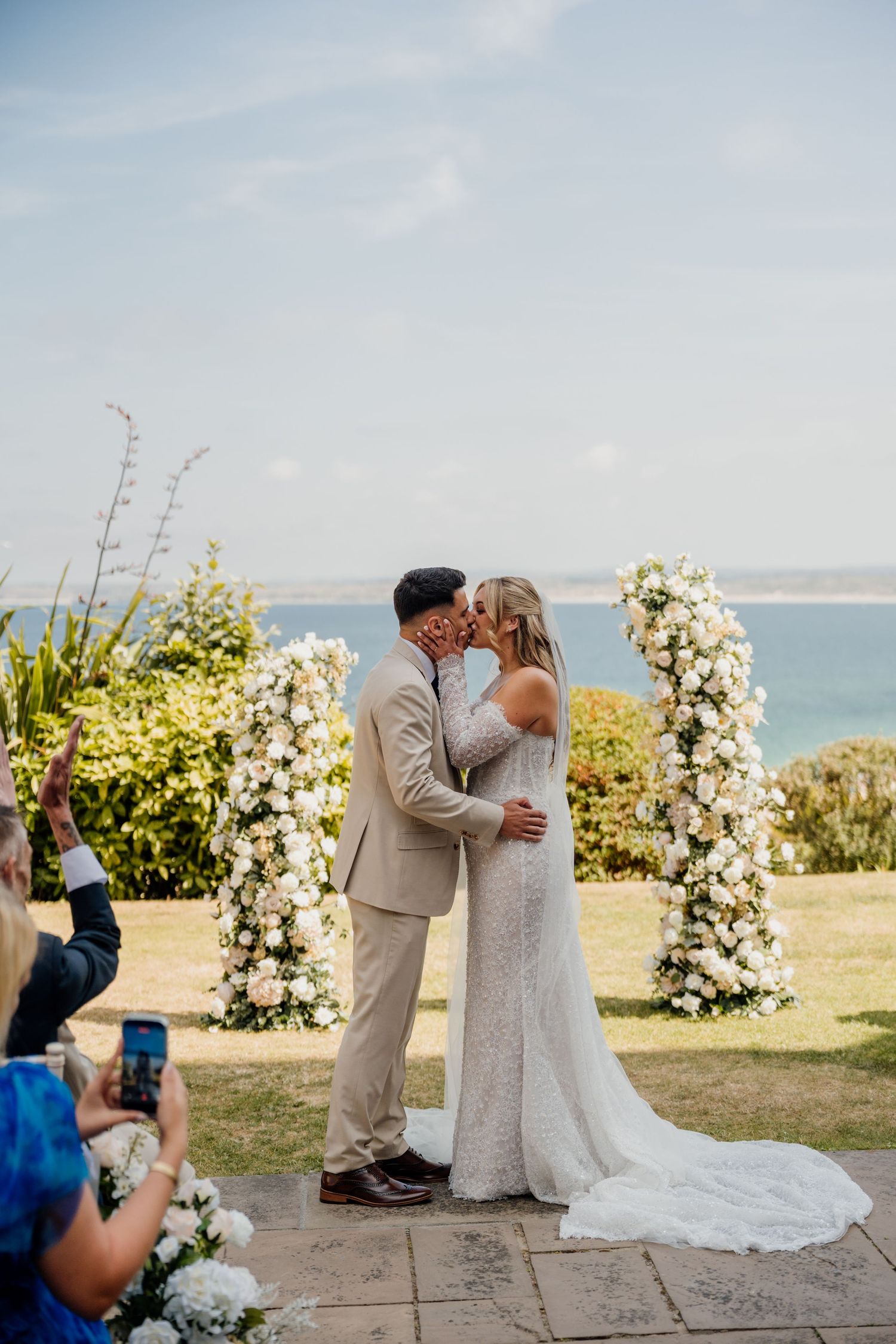 Bride and groom share first kiss at outdoor wedding ceremony at the st ives harbour hotel with floral arch and ocean view backdrop.