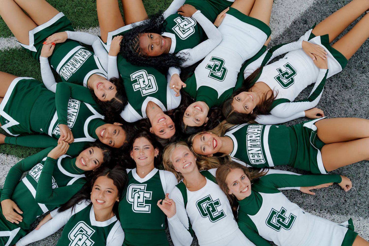 Cheerleaders in green uniforms pose in circle from above.