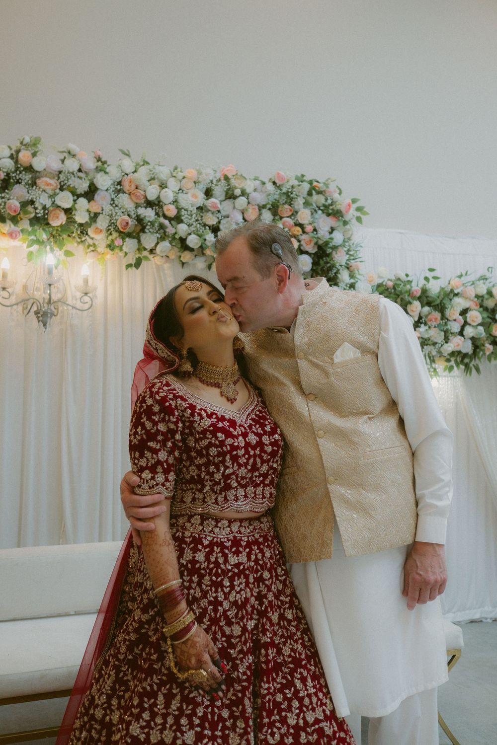 Candid photo of an Indian and English bride being kissed by her father on the wedding day.