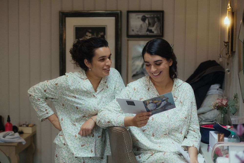 Candid photo of the bride and her sister on the morning of the wedding with matching pyjamas reading a card together.