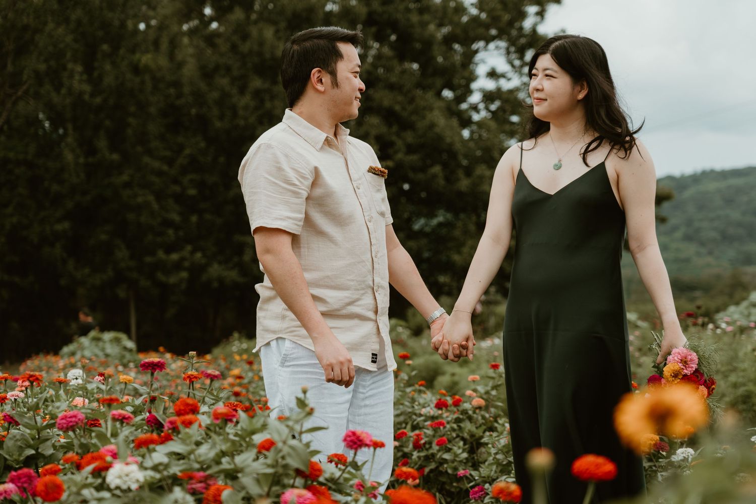 Couple holding hands in a colorful flower field, sharing a romantic moment outdoors.