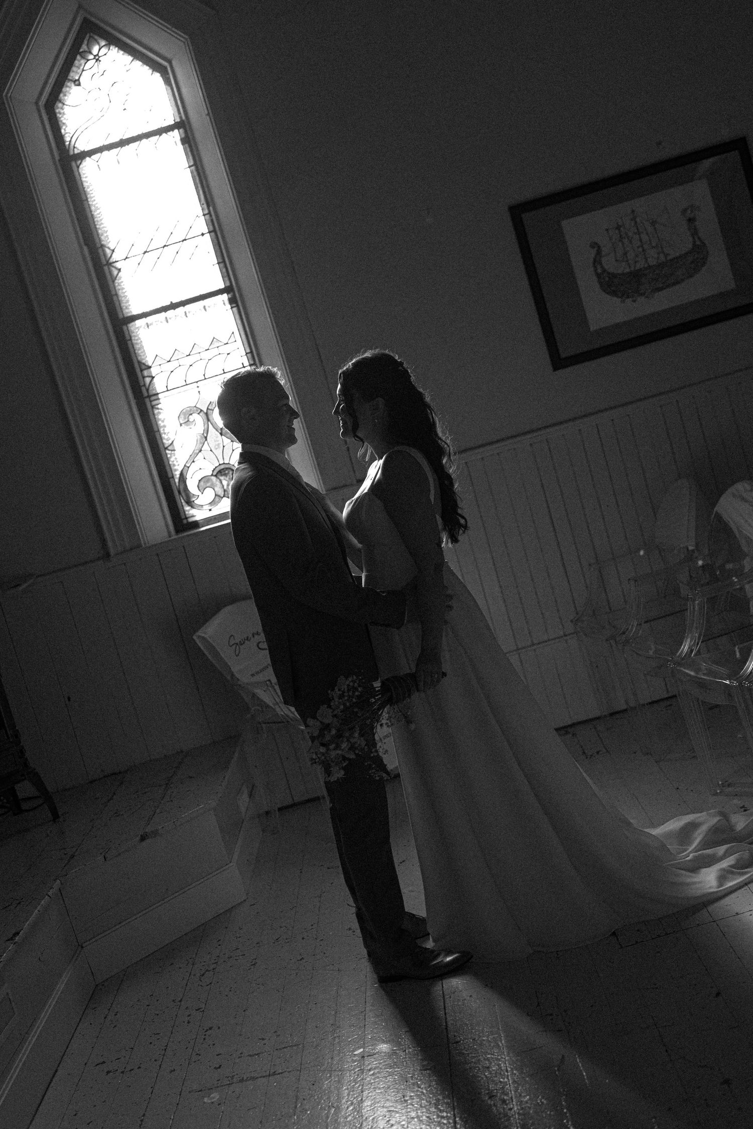 Black and white photo of a bride and groom sharing an intimate moment in a sunlit vintage room.