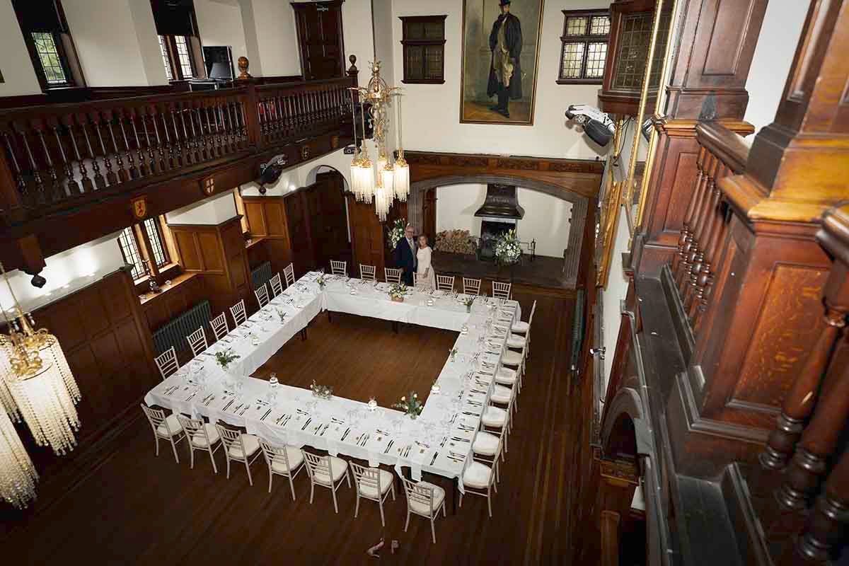 Elegant historic hall with dark wood paneling, chandelier, and U-shaped conference table setup viewed from above.