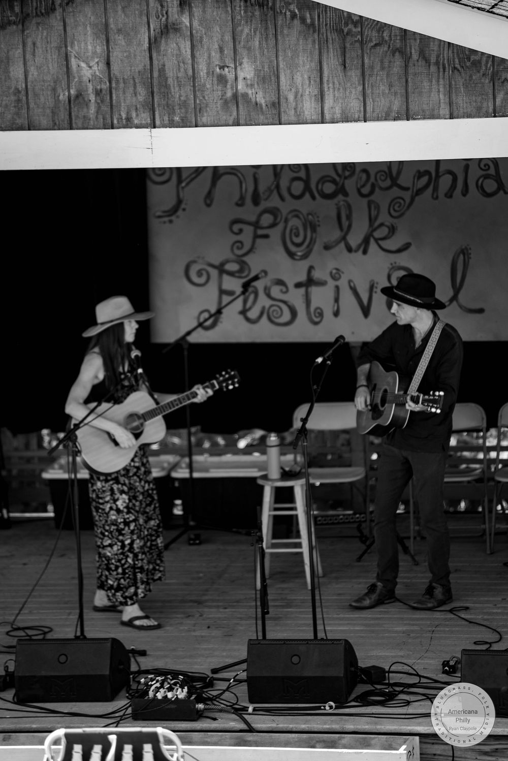 Two musicians perform on stage at Philadelphia Folk Festival, playing acoustic guitars in black and white photo.