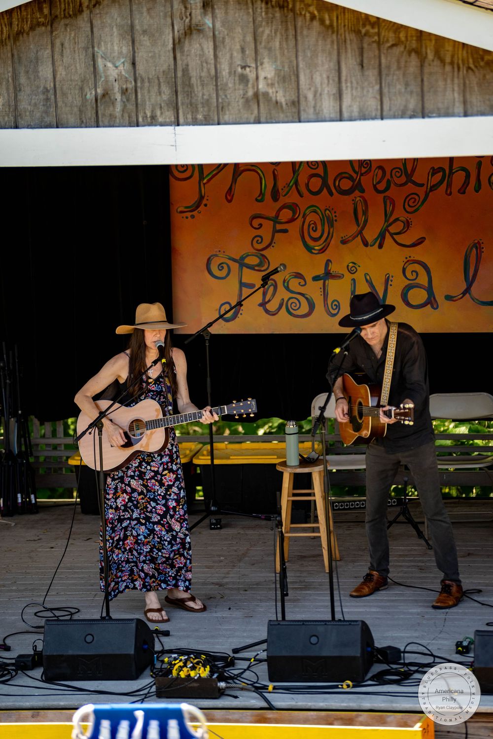 Two musicians perform acoustic guitars on stage at the Philadelphia Folk Festival outdoors.