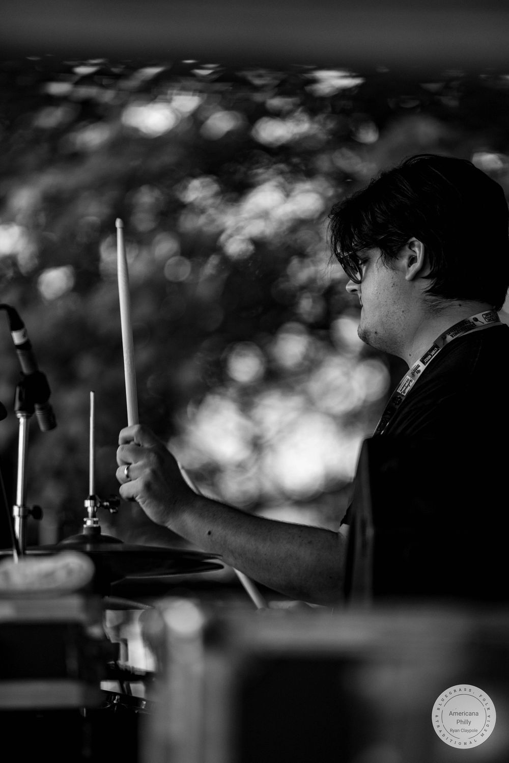 Black and white photo of a drummer playing with drumsticks at an outdoor music event.