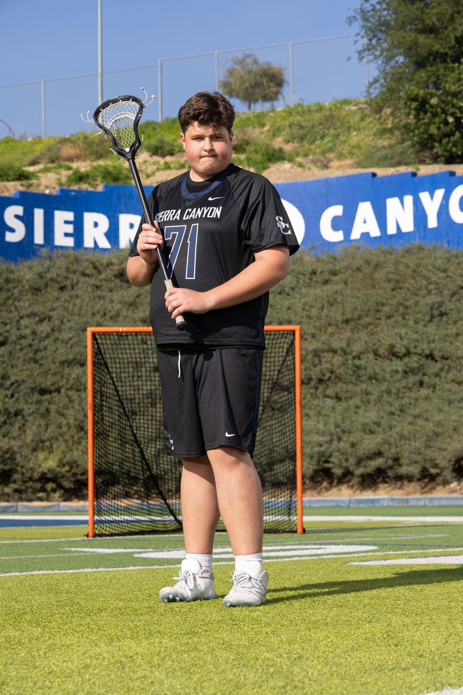 Sierra Canyon lacrosse player #71 poses with stick on turf field in black uniform.