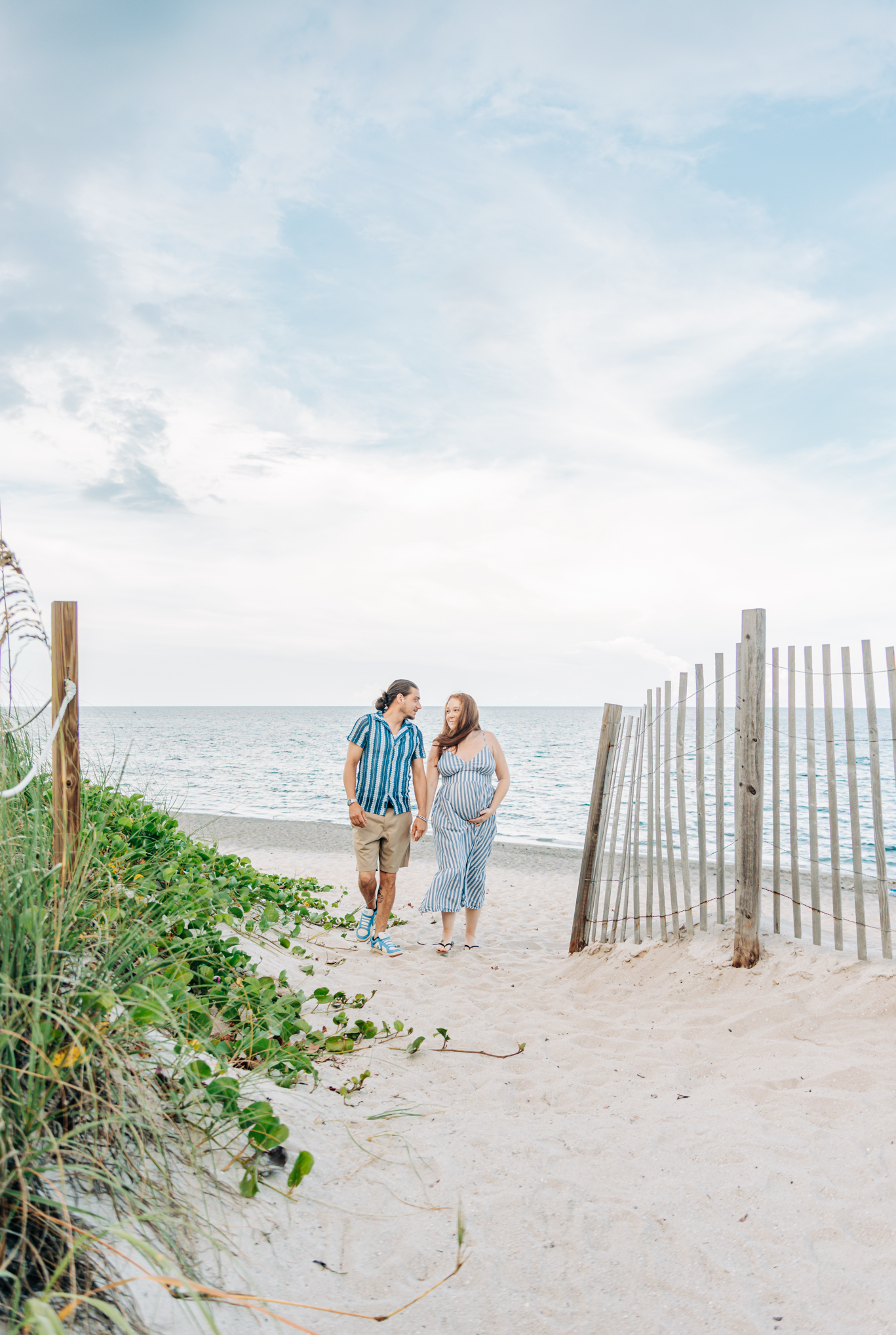 Maternity photoshoot at Coral Cove Beach in Jupiter with an expecting couple walking hand-in-hand toward the ocean.