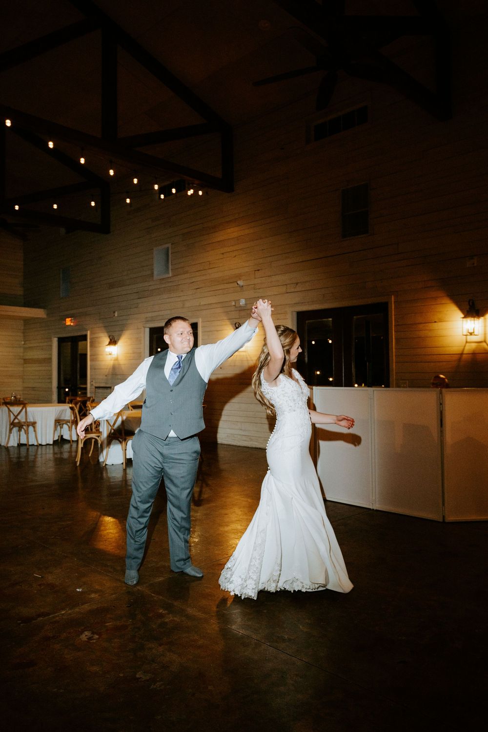 Bride and groom share a joyful first dance as groom twirls bride in a rustic barn wedding reception venue.