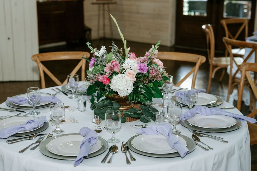 Elegant wedding reception table with lavender napkins, silver chargers, and a floral centerpiece of pink and white blooms.