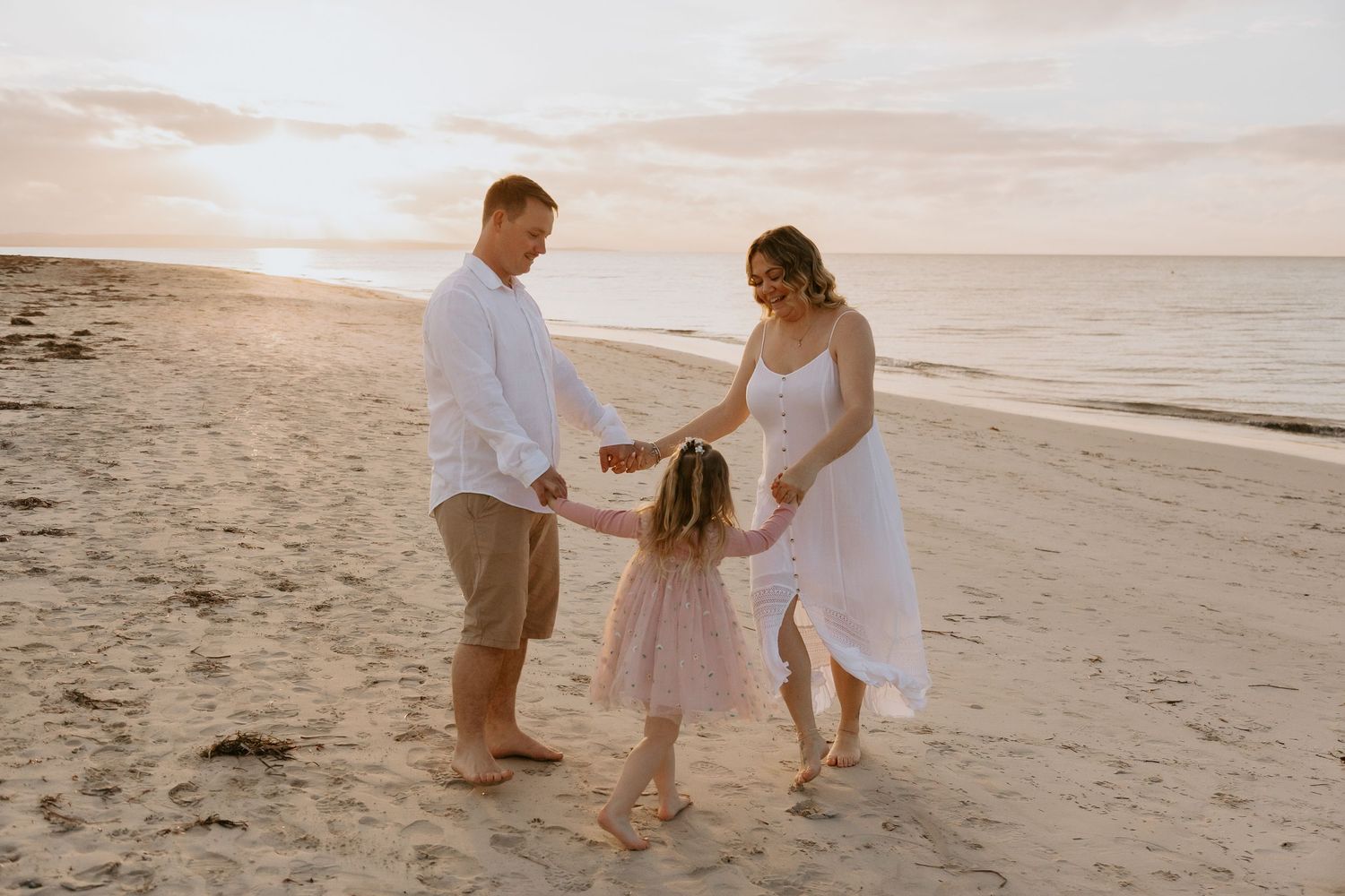 Couple sharing a tender maternity moment at golden hour sunset, man kissing woman's cheek while cradling her baby bump.