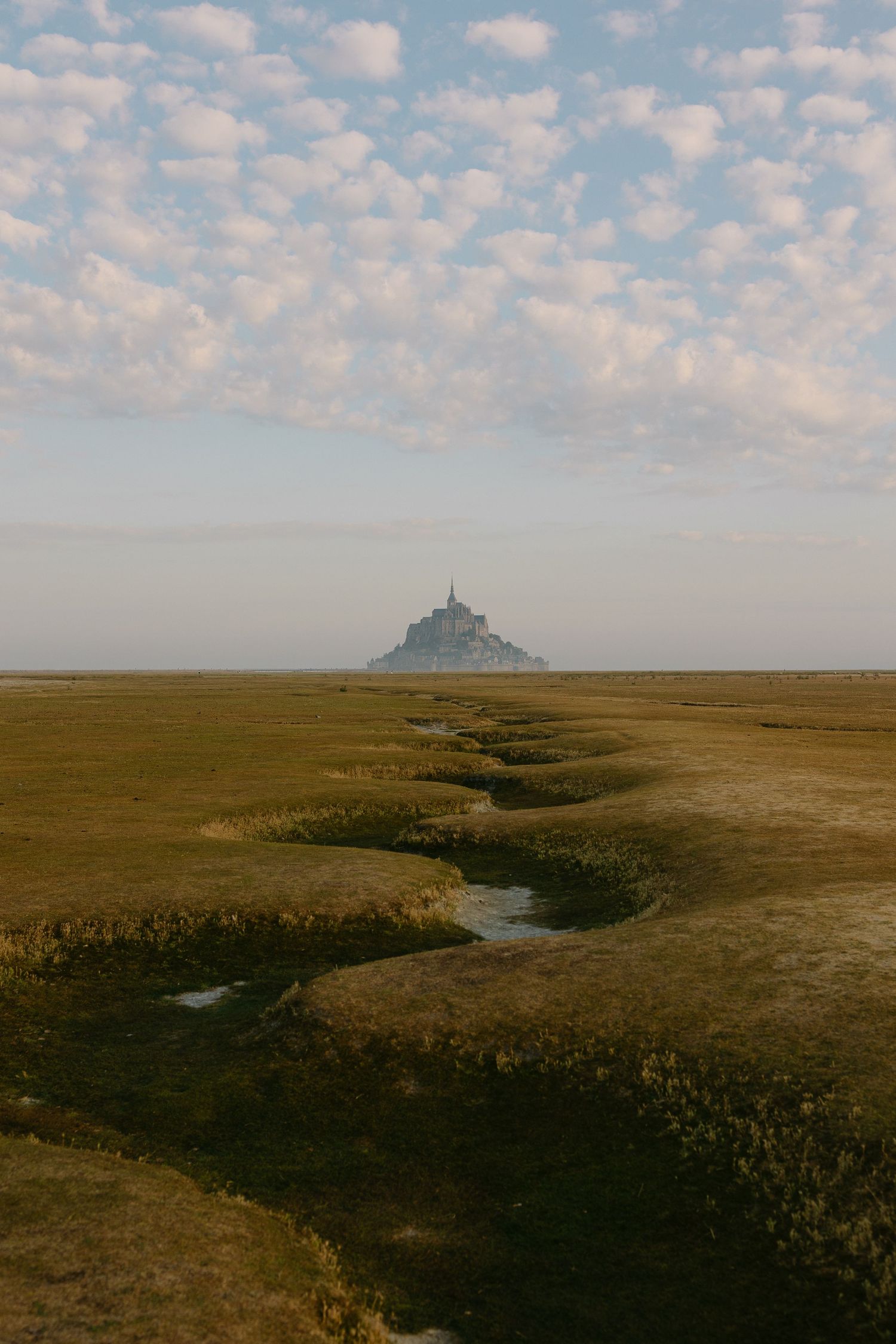 Aerial view of Mont Saint-Michel rising from vast tidal flats under a cloudy sky in Normandy, France.