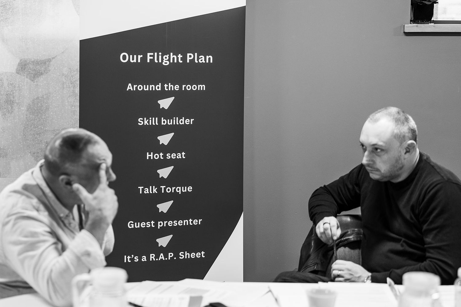 Two men in discussion at business meeting with Our Flight Plan agenda board.