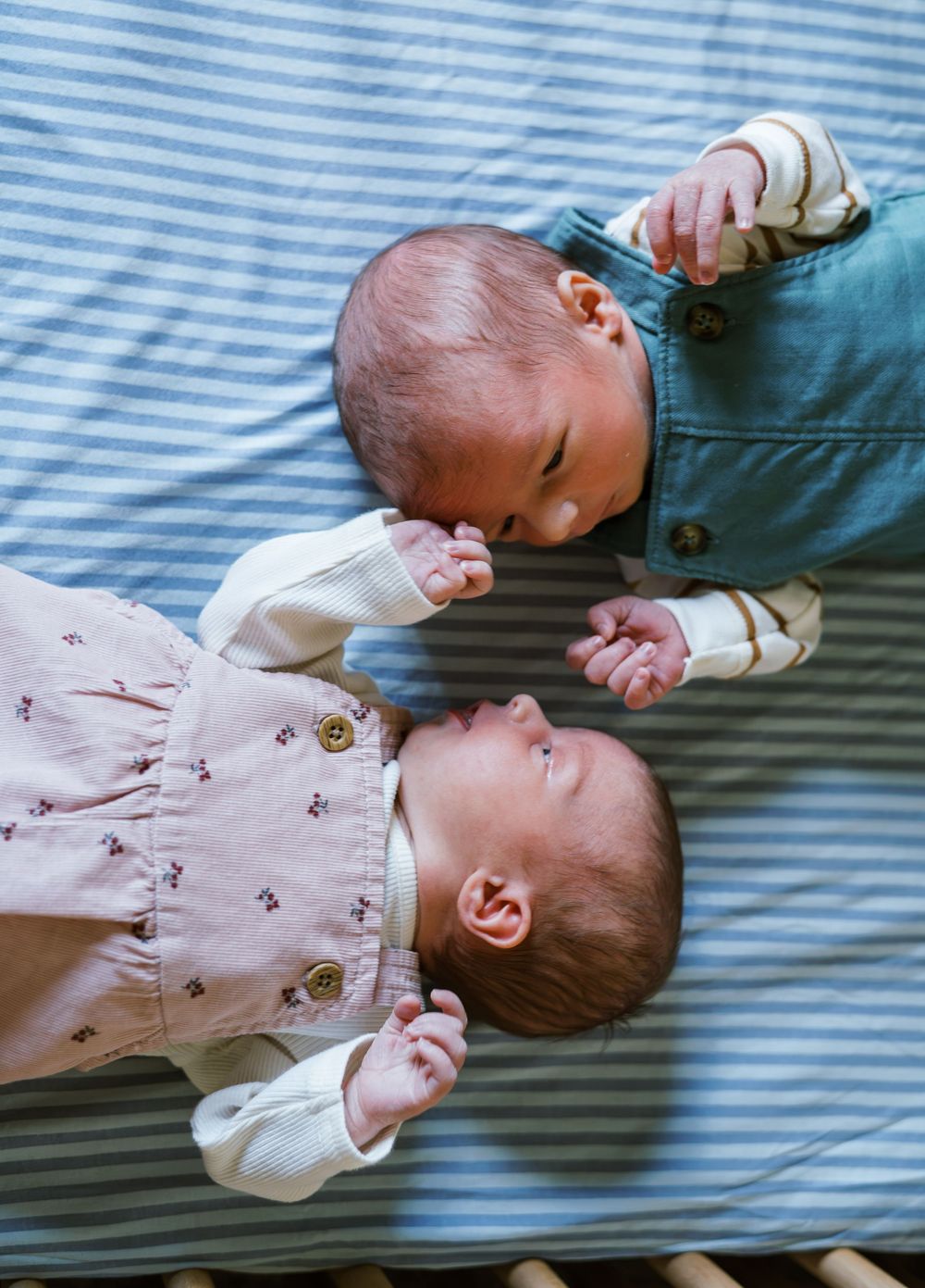 Two newborn babies lying side by side on a striped blue blanket, facing each other.
