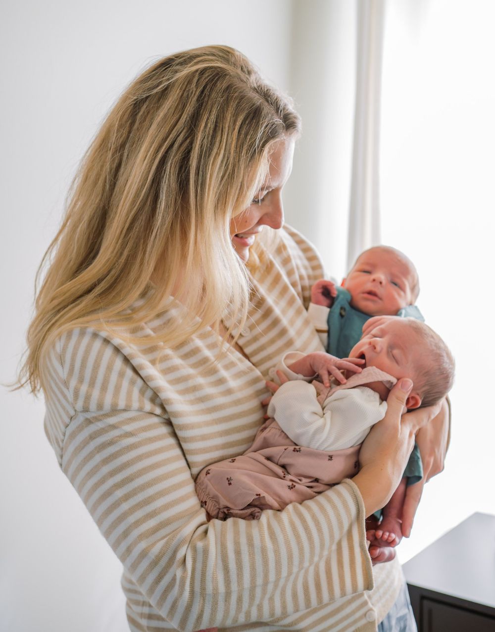 Mother cradling two newborn twins in her arms, gazing down at them tenderly.
