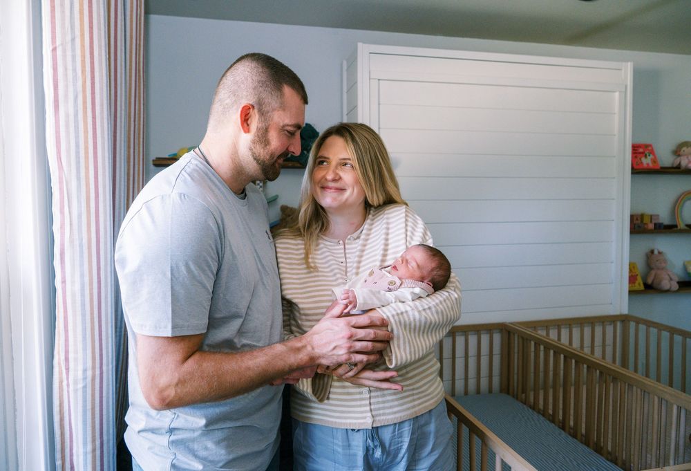 New parents smiling and holding their newborn baby in a cozy nursery room.