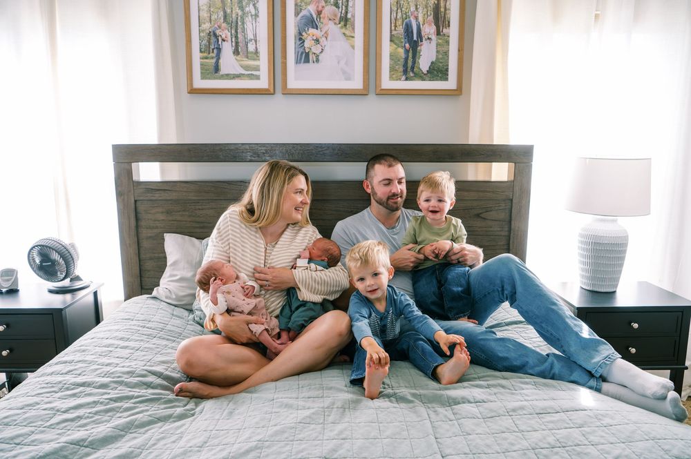 Happy family with newborn baby and two young children sitting together on a bed in a cozy bedroom.