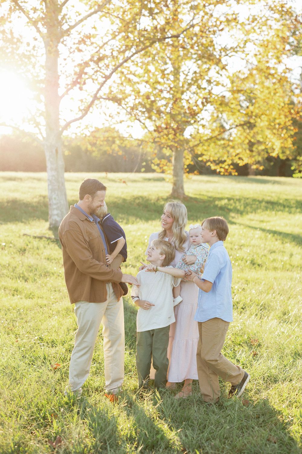 A joyful family of five shares a warm moment in a sunlit park during golden hour autumn afternoon.