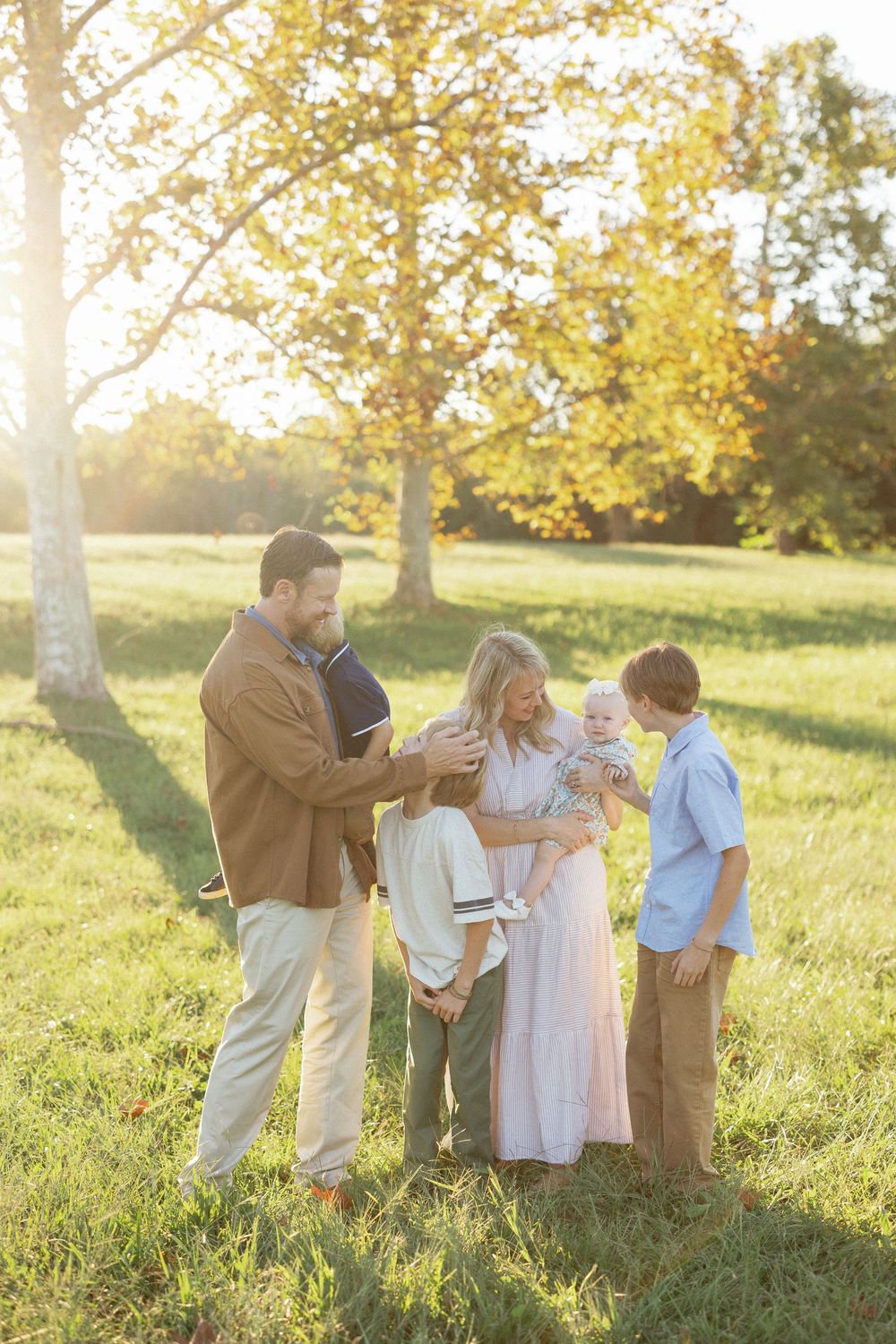 Family of five sharing a joyful moment together in a sunlit green field during golden hour.