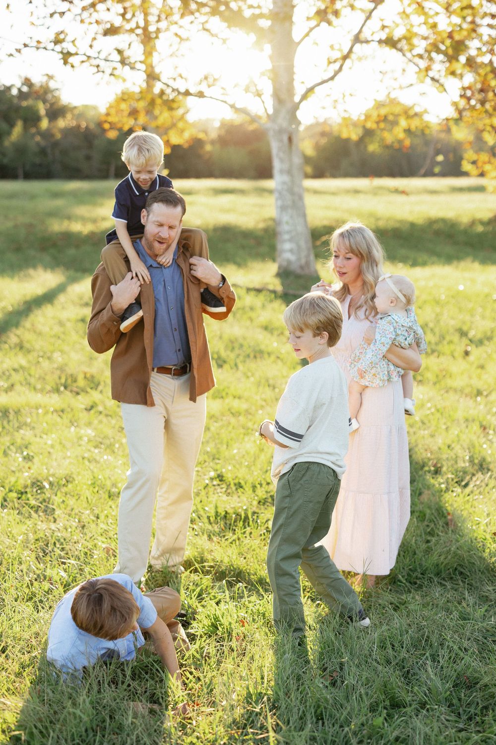 Family of six enjoying a sunny outdoor photo session in a green field with golden backlight.