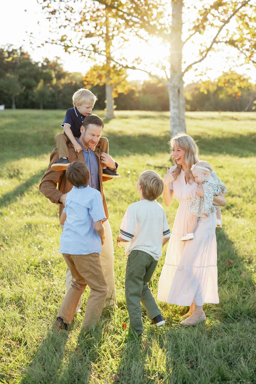 Happy family of six enjoying a sunny outdoor photo session in a green park during golden hour.