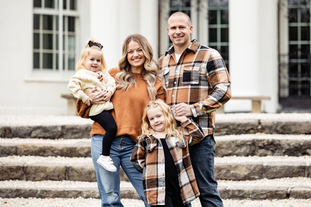 Happy family of four posing outdoors in matching plaid flannel shirts for a fall family portrait photo.
