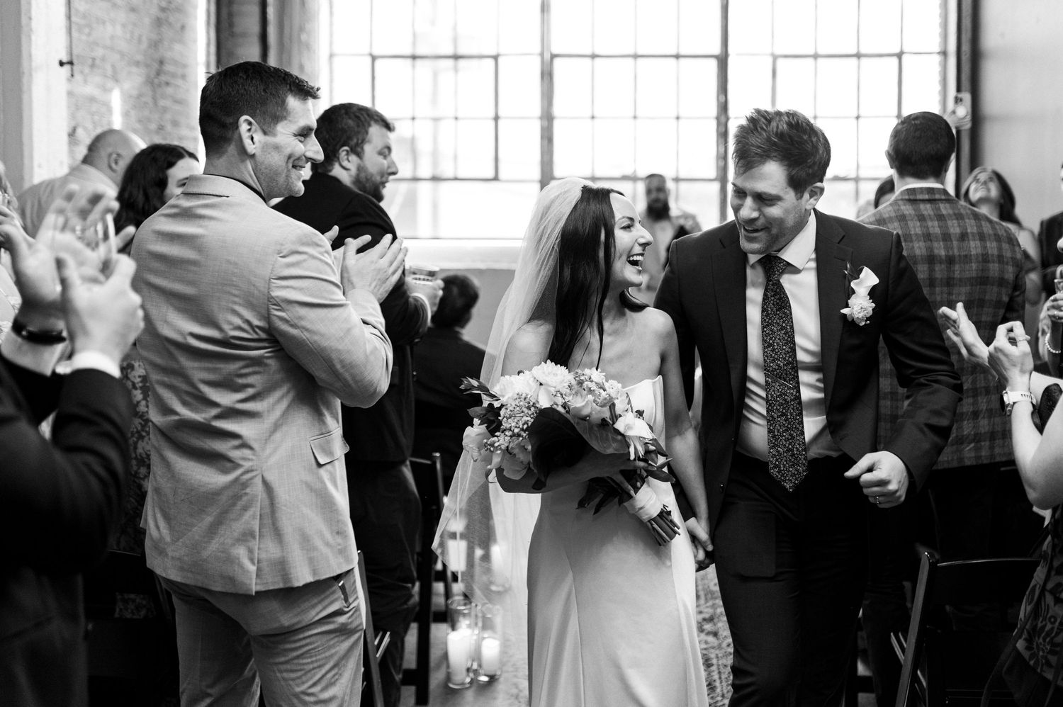 Black and white photo of a joyful bride and groom walking down the aisle at their wedding ceremony.