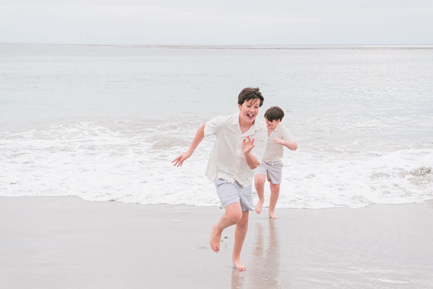 run together along a sandy beach with ocean waves in the background. Carmel-by-the-Sea family photographer