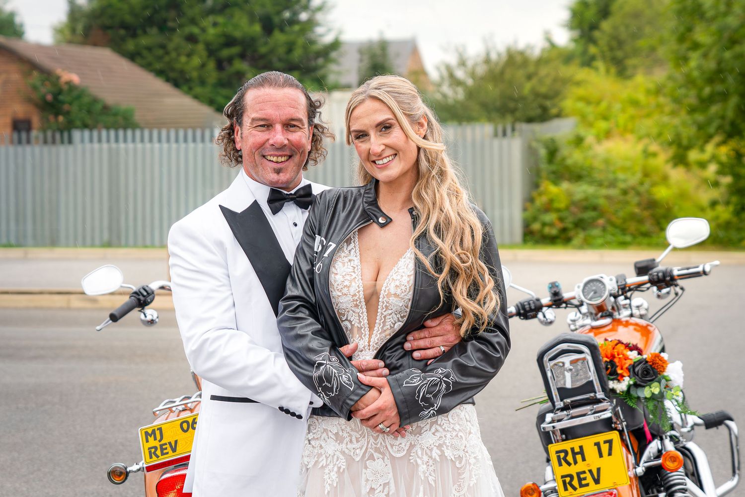 Bride and groom pose together in wedding attire beside motorcycles on a sunny wedding venue.Yorkshire, Sheffield, Lincolnshire, UK