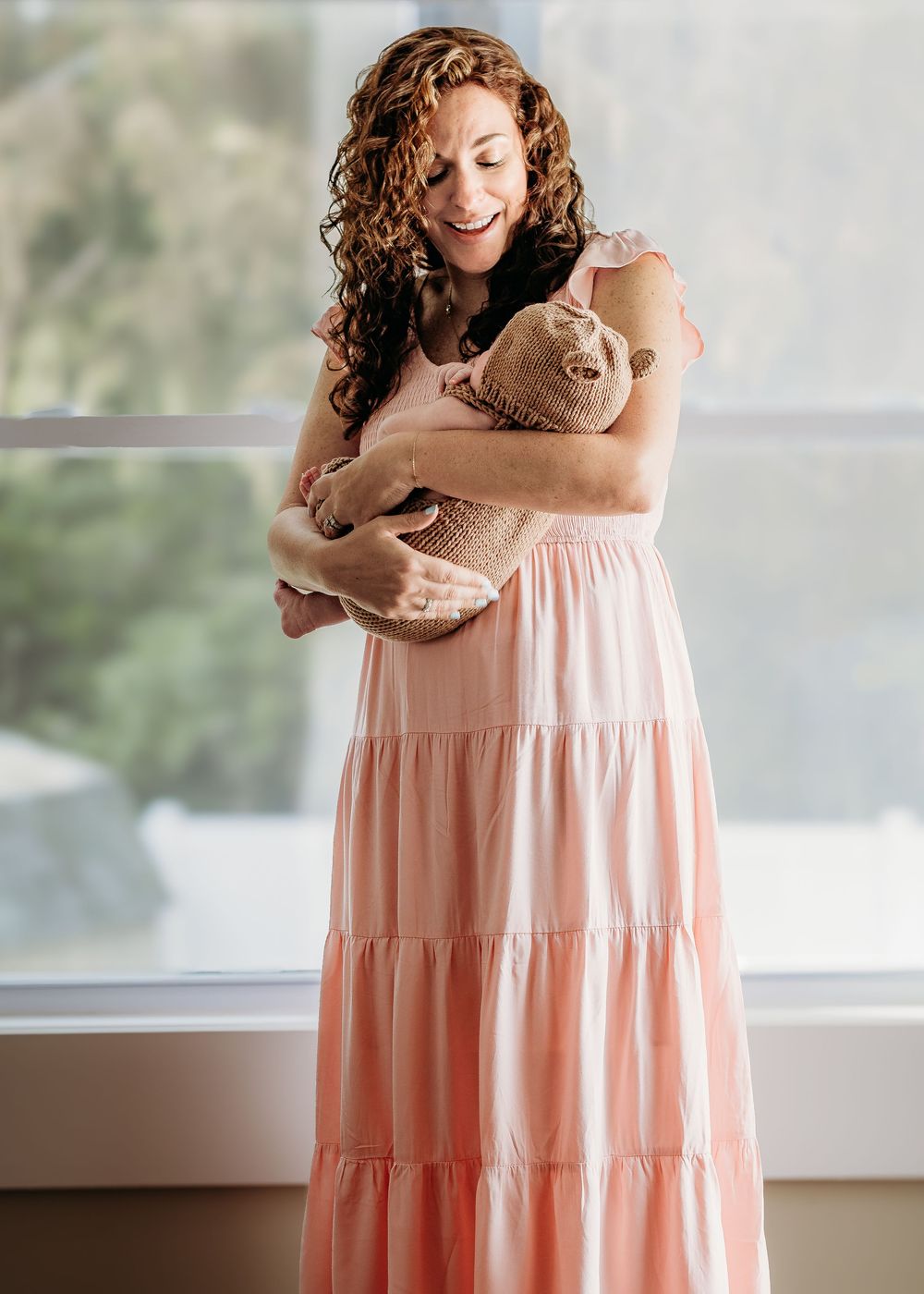 Mother holding her newborn baby by the window during an in-home newborn photography session.