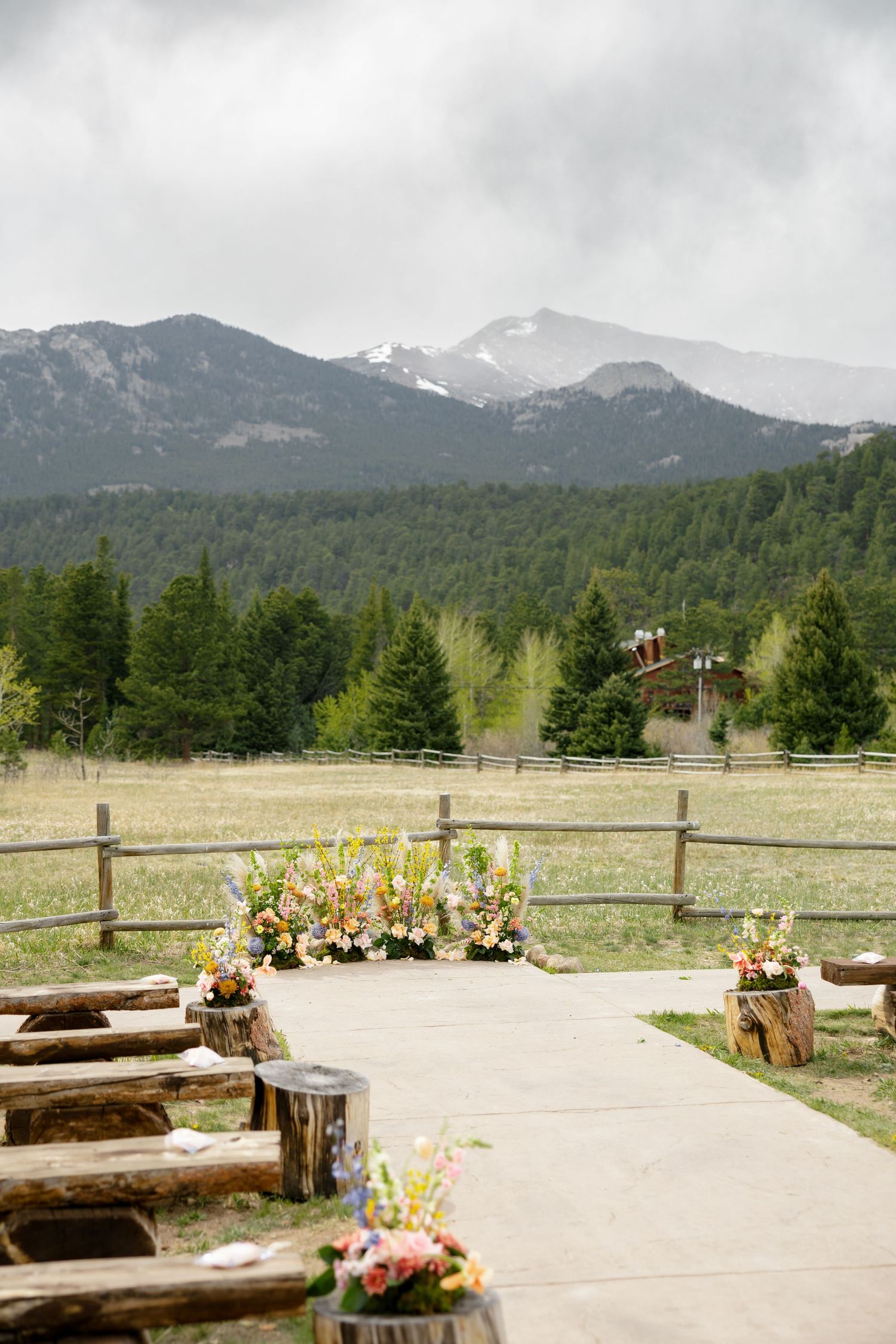 Rustic outdoor wedding ceremony setup with wooden benches, floral arrangements, and stunning Rocky Mountain backdrop.