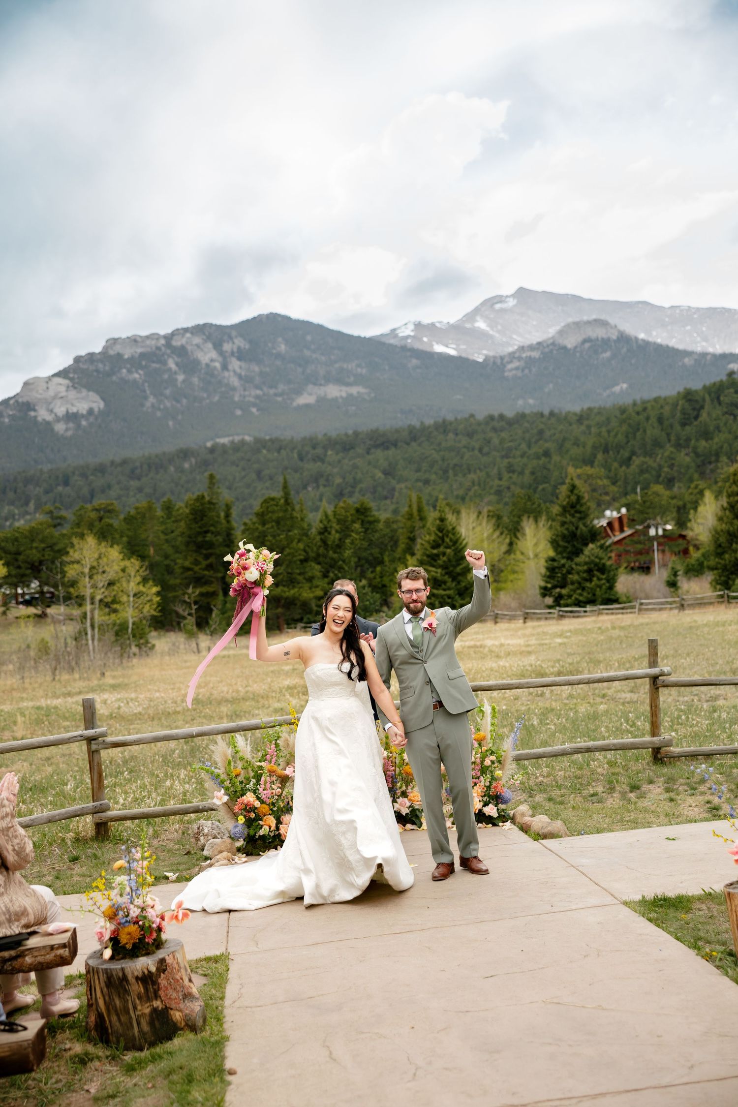 Joyful newlyweds celebrate after outdoor mountain wedding ceremony with floral bouquet and snow-capped peaks backdrop.