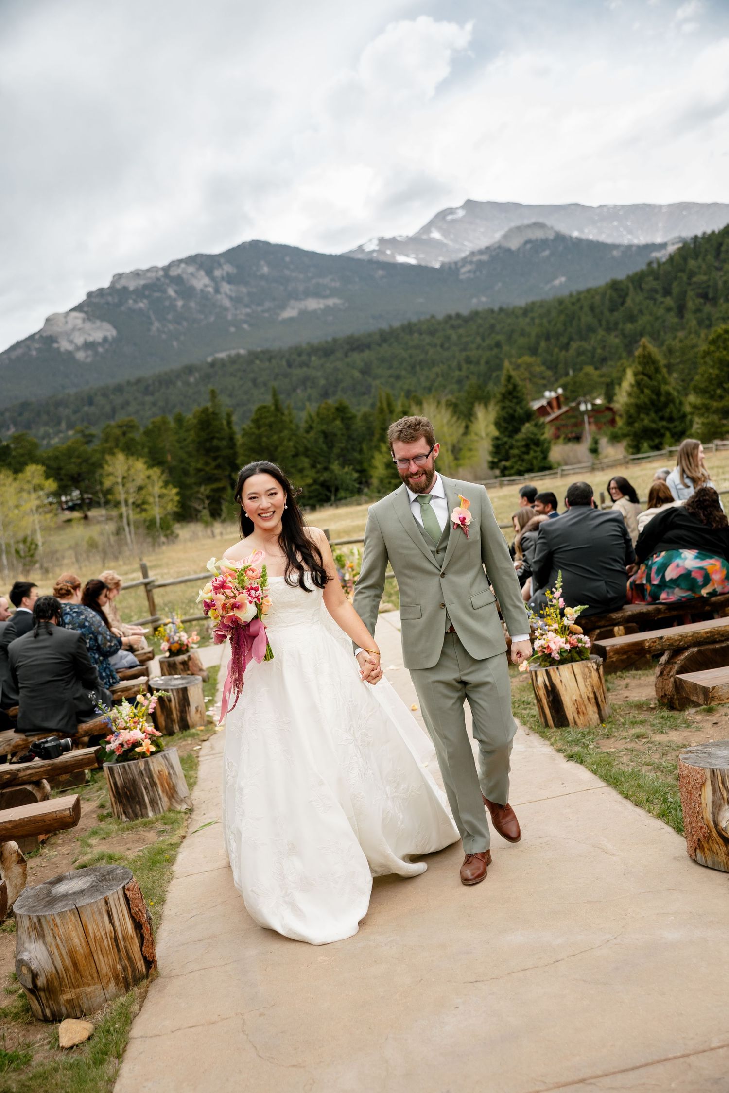 Bride and groom walk down outdoor aisle with mountain backdrop at Rocky Mountain wedding ceremony.