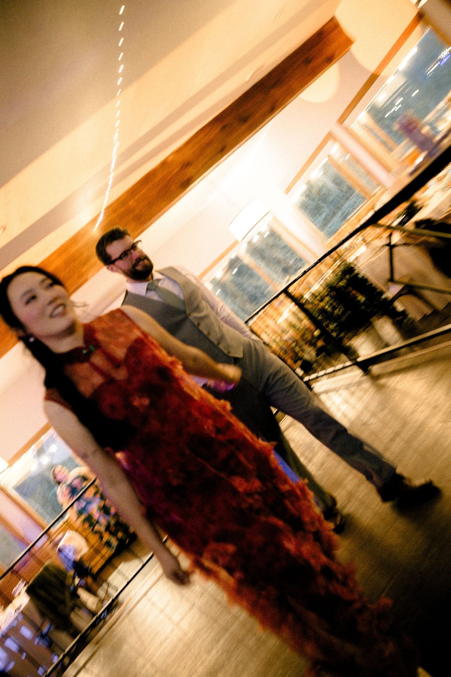 A smiling woman in a red floral dress poses with a man in a suit at an indoor event venue.