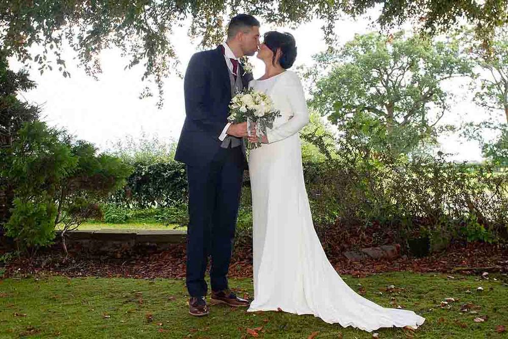 Bride and groom sharing a romantic moment in a lush garden, bride in elegant white gown holding a bouquet.