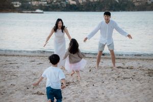Family of four joyfully running on a sandy beach at sunset, with parents welcoming their children with open arms.