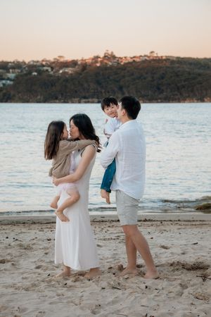 A happy Asian family of four shares a tender moment on a serene beach at golden hour.
