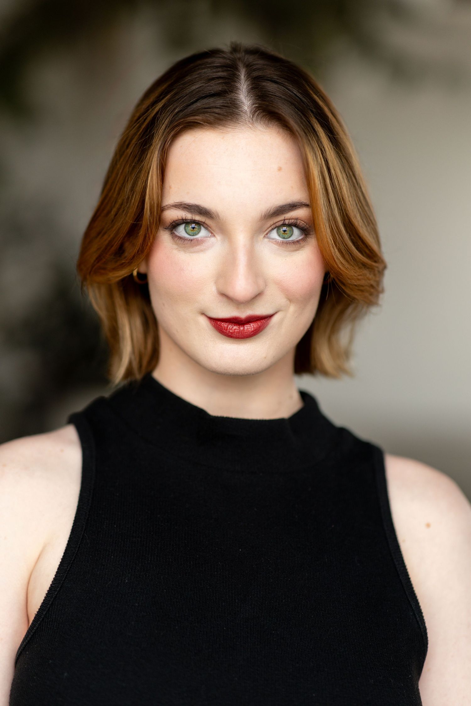 Professional headshot against blurred background featuring black high neck top.