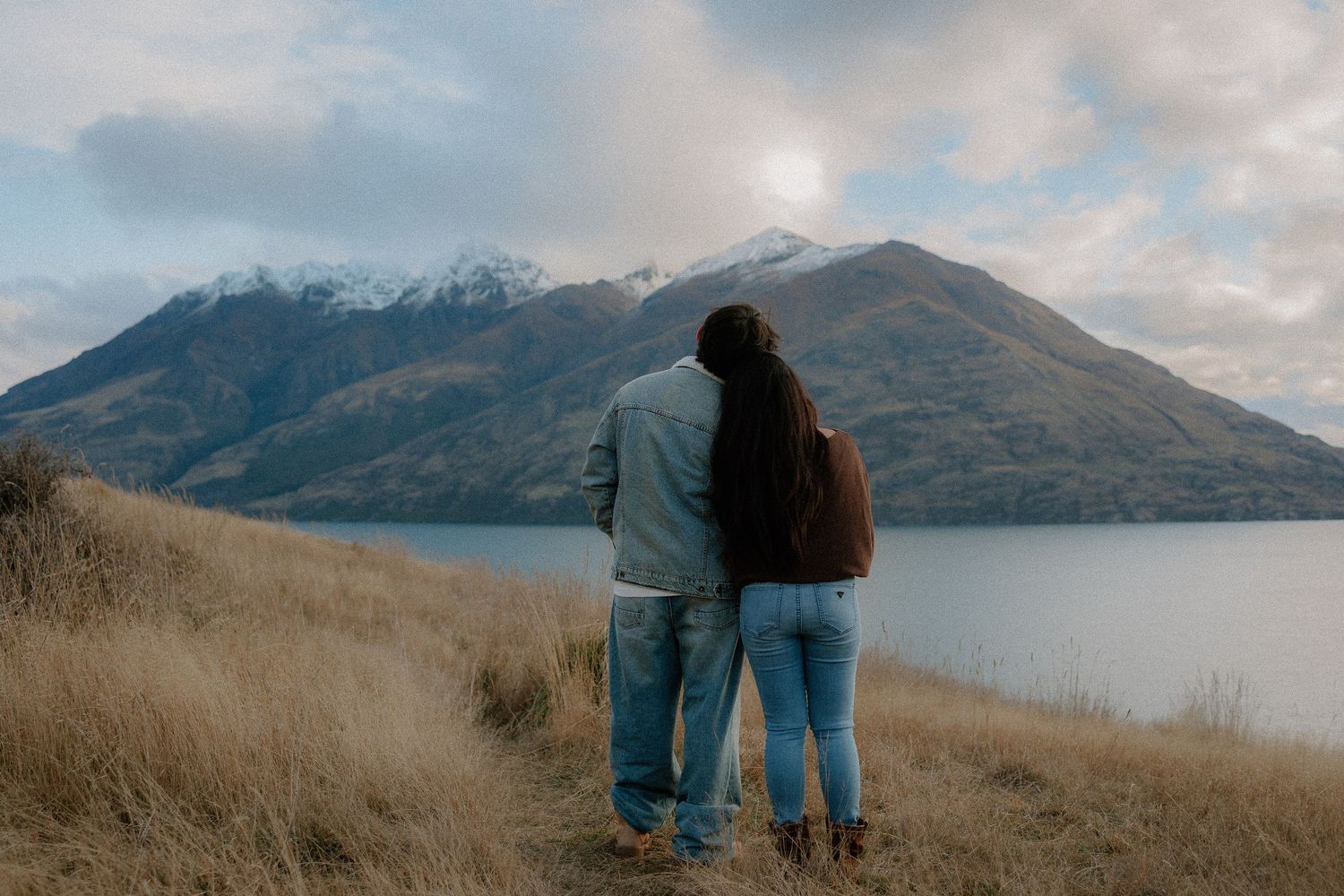 A couple enjoying views of Lake Wakatipu  with snow-capped mountains in the background.