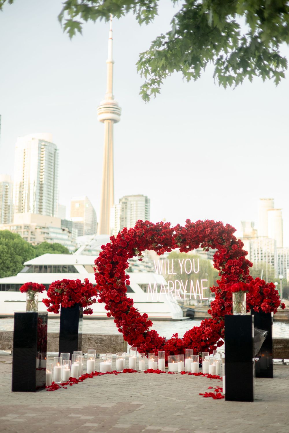 Stunning marriage proposal setup with red rose heart arch, CN Tower backdrop, and candlelit pathway.
