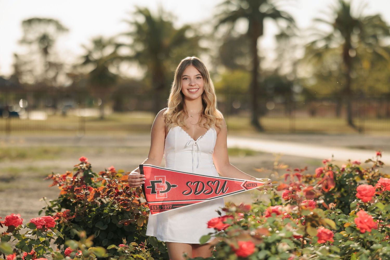 senior girl holding her SDSU pennant in the rose garden in Tucson, AZ