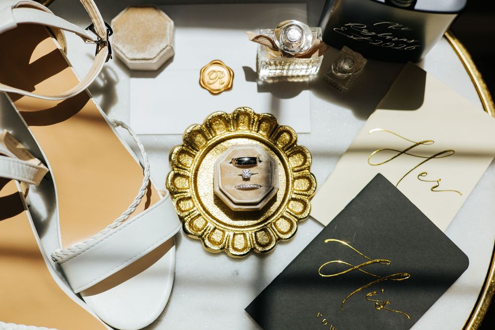 Wedding flat lay with gold ring dish, heels, stationery, and accessories.
