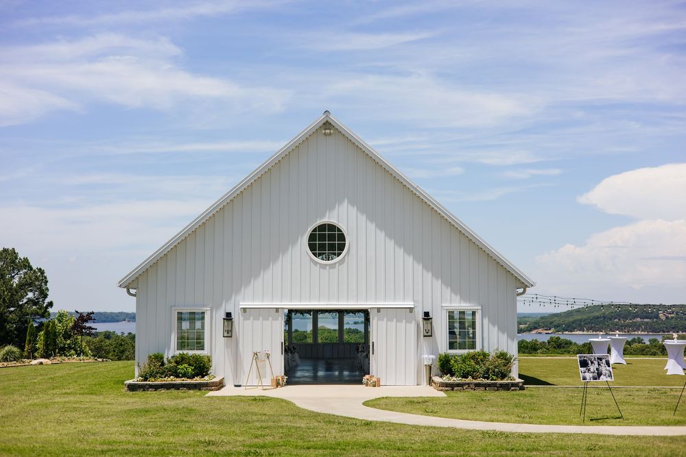 White barn-style wedding venue with circular window set against a blue sky near the water.