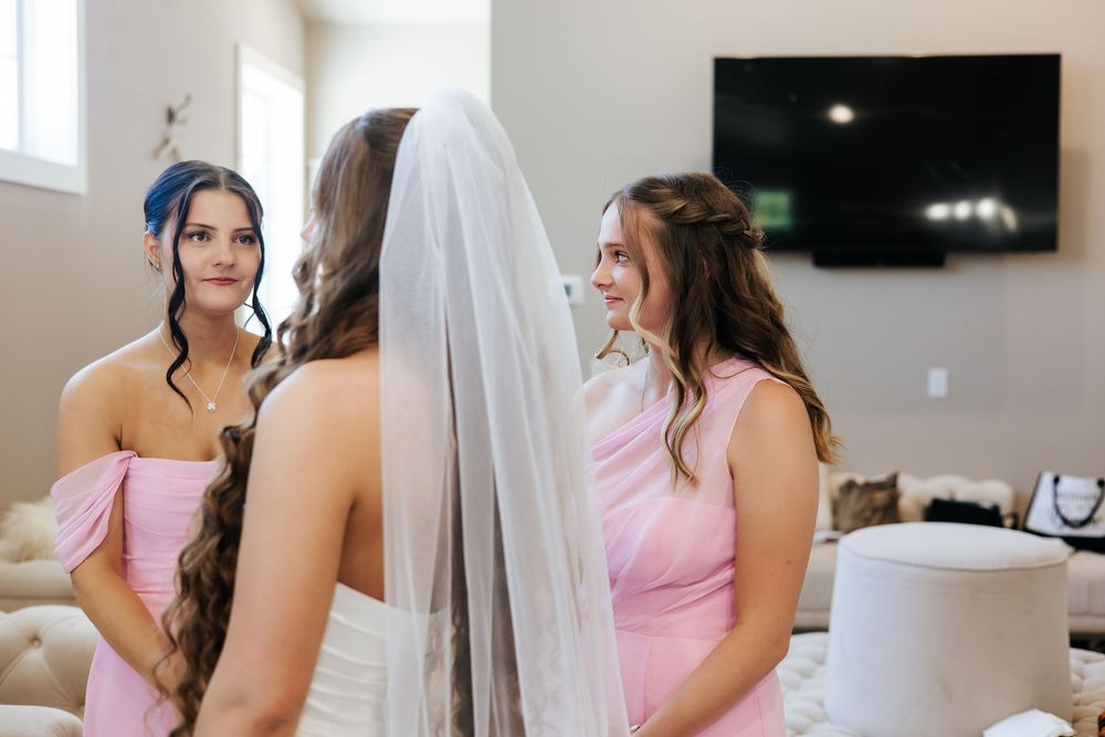 Bride in veil sharing tender moment with bridesmaids in pink dresses before wedding.
