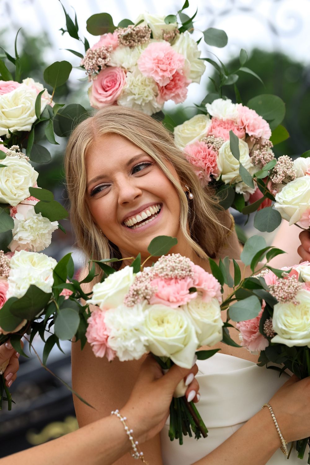 Smiling bride surrounded by pink and white rose bouquets with eucalyptus greenery on her wedding day.