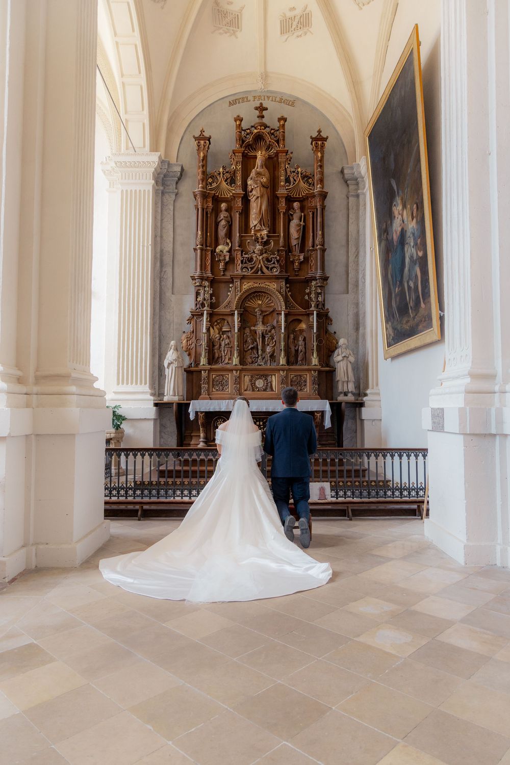 Bride and groom standing before ornate golden altar in elegant white church during wedding ceremony.