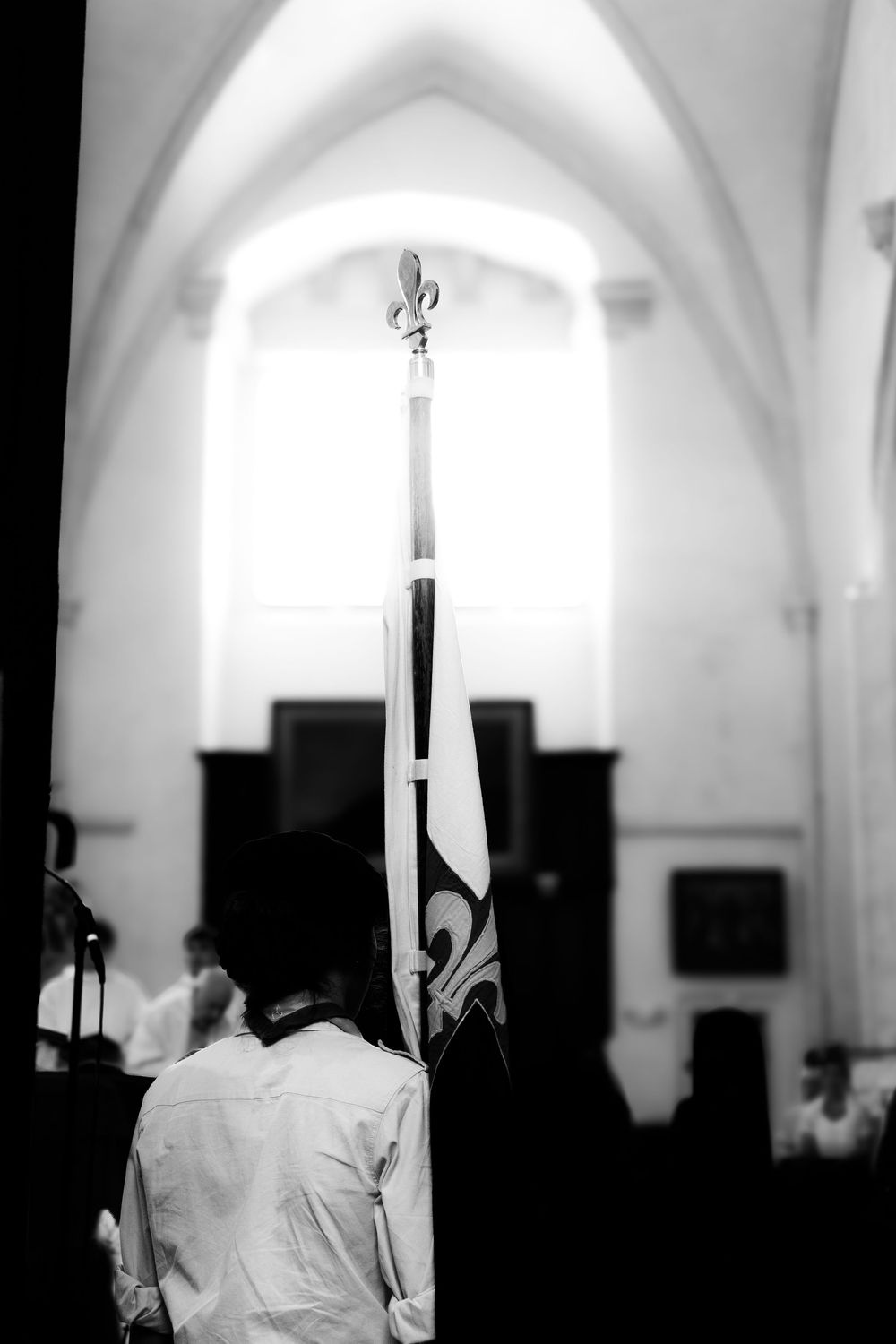 Black and white photo of a person holding a ceremonial flag with fleur-de-lis inside a grand church.