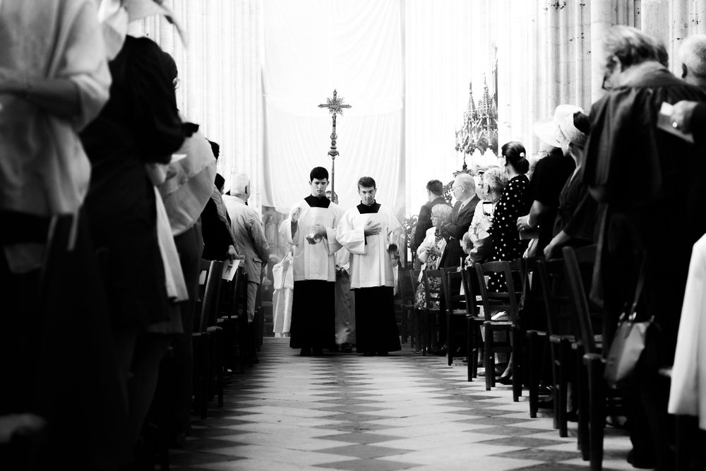 Black and white photo of a church procession with clergy walking down the aisle of a grand cathedral.