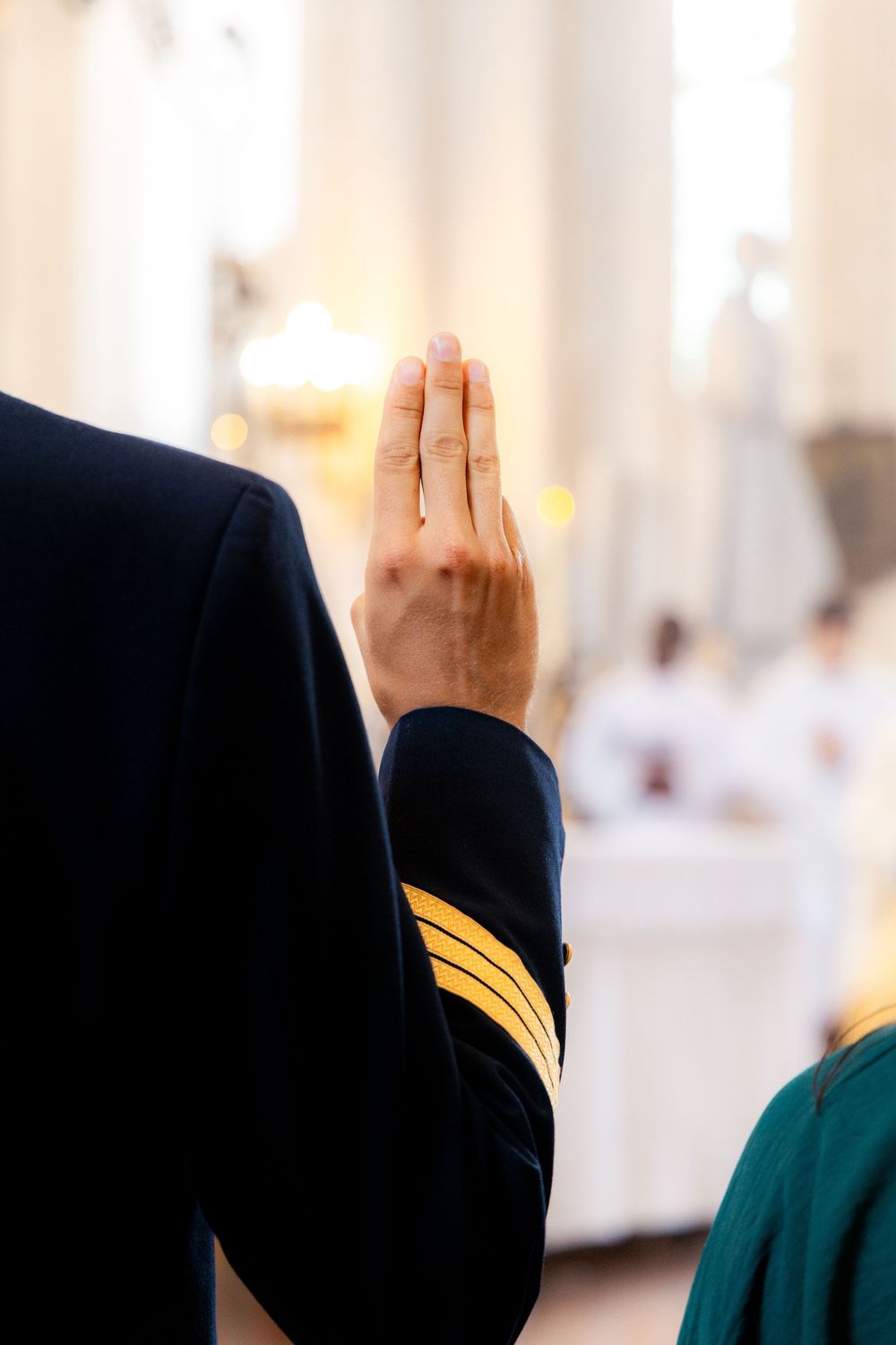 Close-up of man in navy uniform with gold stripes raising hand during a solemn church wedding vow ceremony.